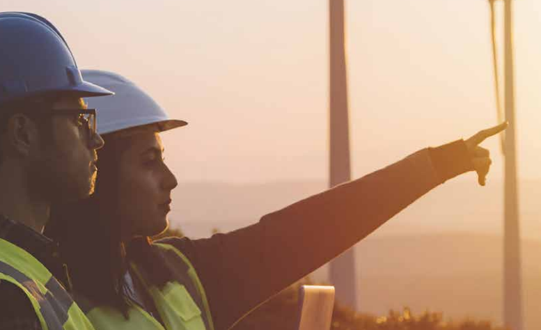 A man and a woman wearing hard hats pointing at a wind turbine